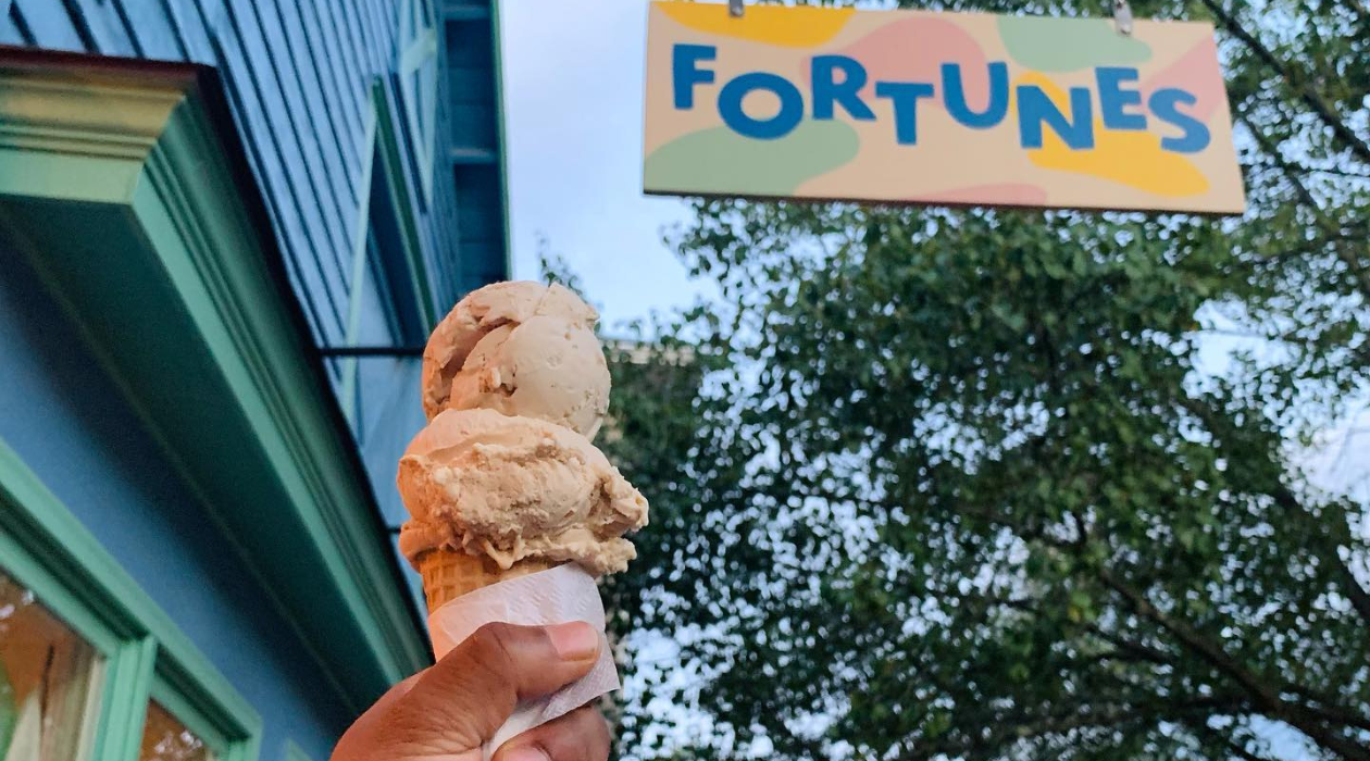 holding an ice cream cone in front of retro style Fortunes Ice Cream sign